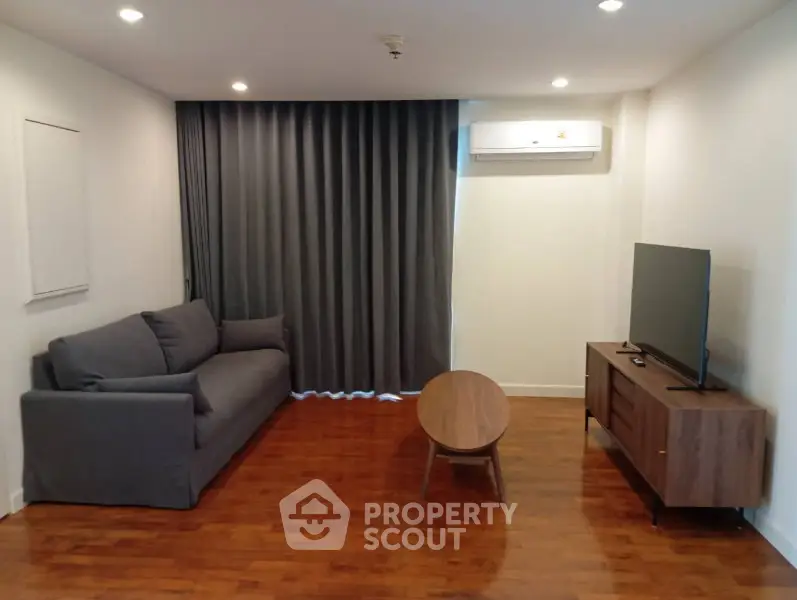 Modern living room with sleek furniture and wooden flooring, featuring a cozy sofa and flat-screen TV.
