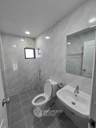Modern bathroom with sleek fixtures and tiled walls, featuring a toilet, sink, and window for natural light.