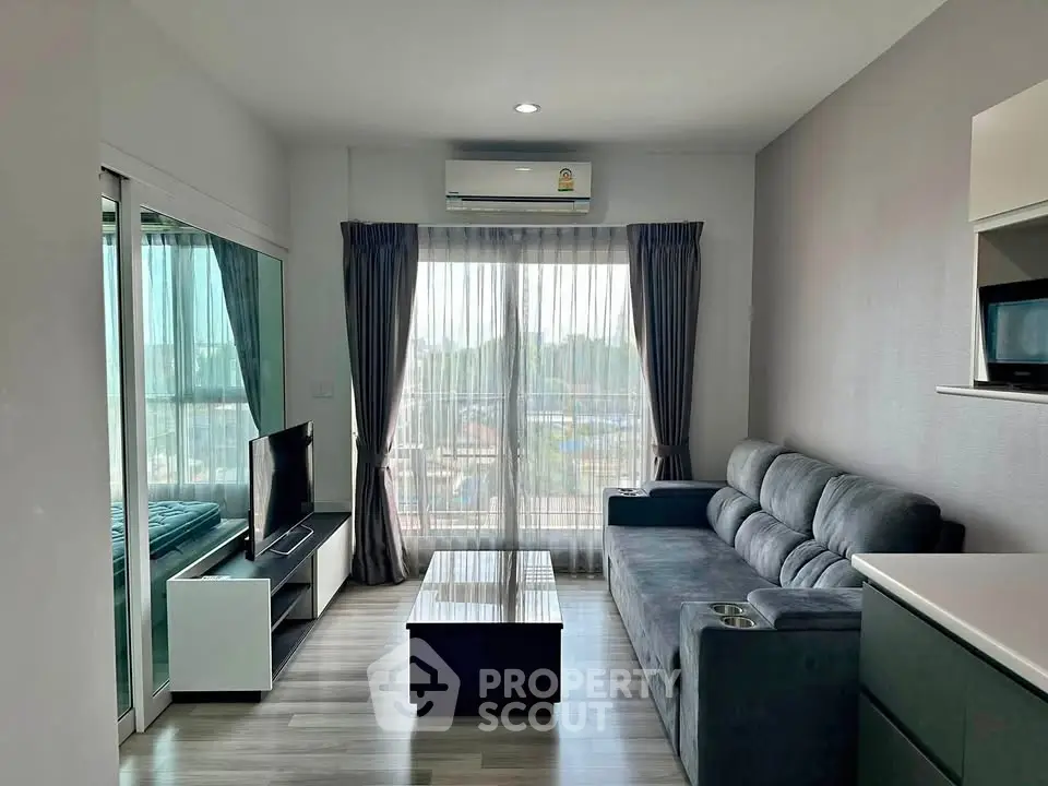 Modern living room with sleek furniture and large window offering natural light and city view.