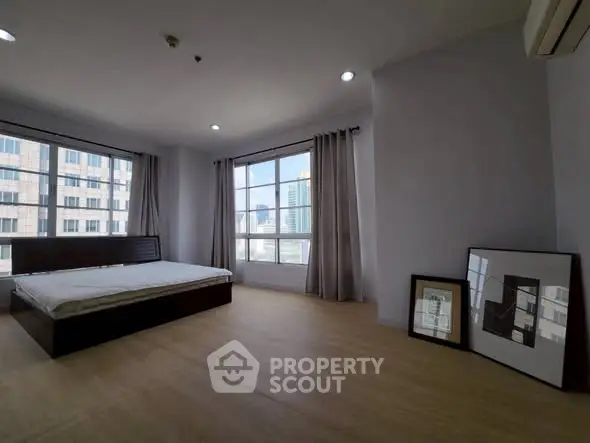 Spacious bedroom with large windows offering city views in modern apartment.