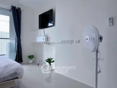 Modern bedroom with sleek design, featuring a wall-mounted TV, standing fan, and large window with city view.