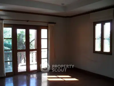 Spacious room with wooden floors and large windows offering natural light and garden view.