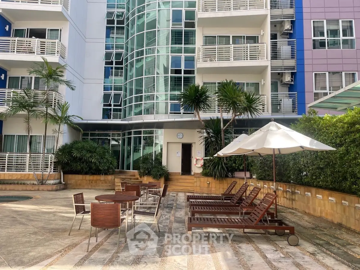 Modern apartment building with poolside seating and lush greenery.