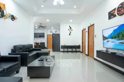 Spacious modern living room with sleek black furniture and wall-mounted TV, leading to a stylish kitchen.