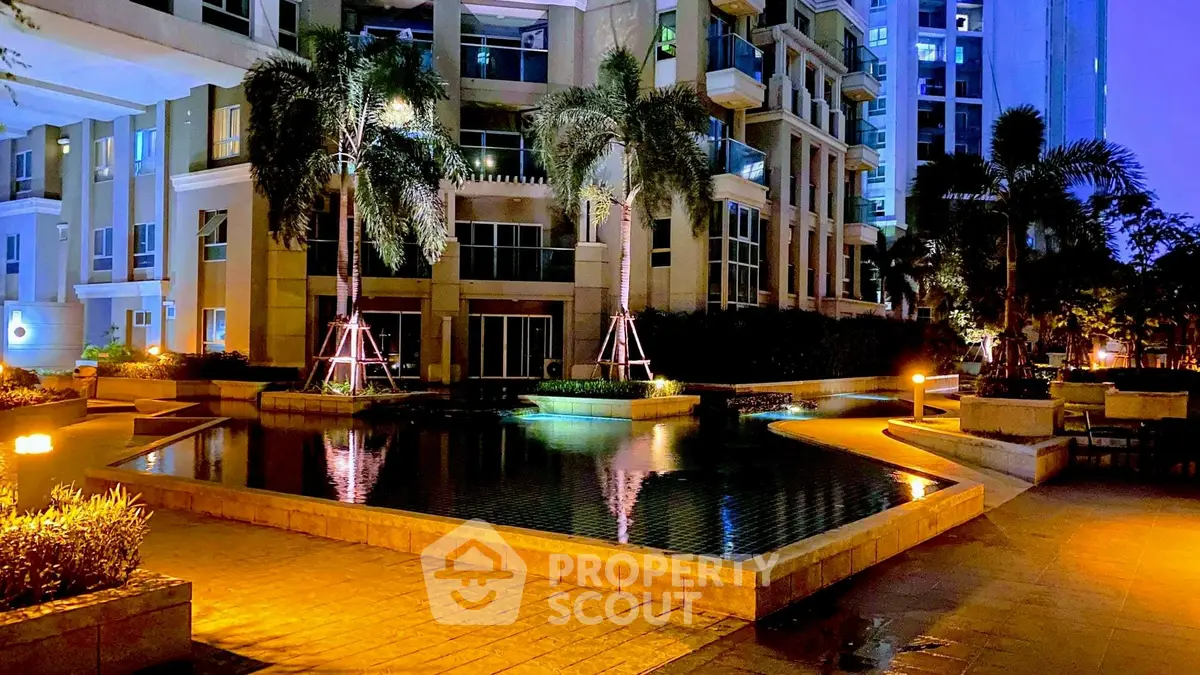 Luxurious apartment complex with illuminated pool and lush greenery at night.