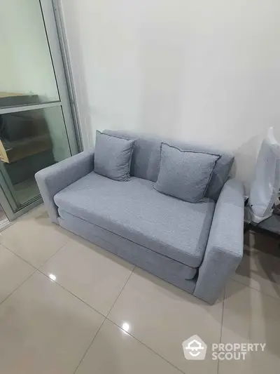 Modern gray sofa in a stylish living room with glossy tiled flooring and glass door.