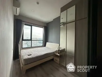 Modern bedroom with large window and city view, featuring sleek furniture and ample natural light.