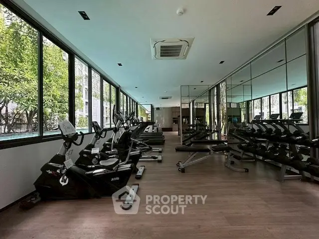 Spacious gym with modern equipment and large windows offering a serene garden view.