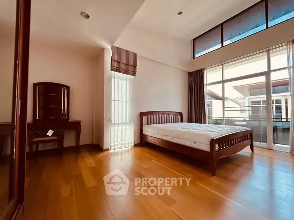 Spacious bedroom with wooden flooring and large windows for natural light.