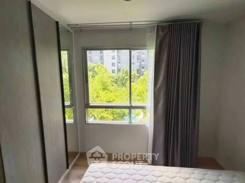 Bright bedroom with large window and greenery view, featuring a comfortable mattress and sleek wardrobe.