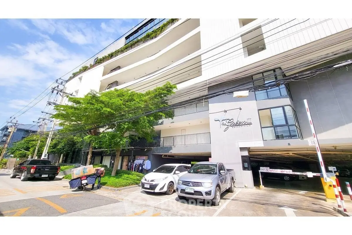 Modern apartment building with parking area and lush greenery in urban setting.