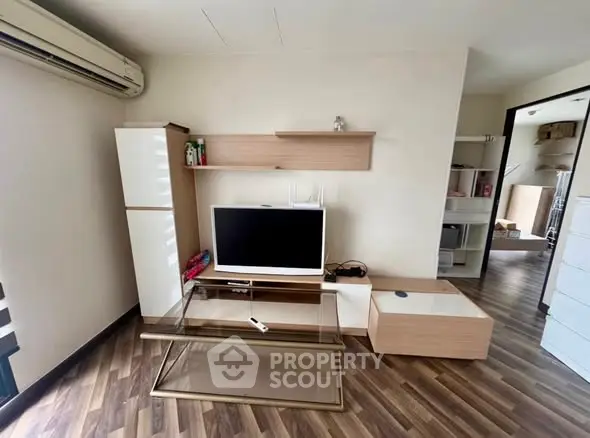 Modern living room with sleek furniture and wooden flooring, featuring a flat-screen TV and stylish shelving.