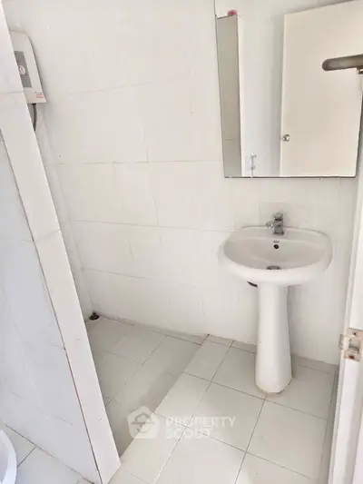 Compact bathroom with pedestal sink and white tiles, ideal for minimalist design.