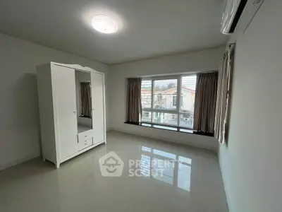 Spacious bedroom with large window and white wardrobe, offering ample natural light.