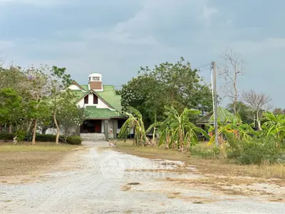 Charming countryside house with green roof surrounded by lush trees and a gravel driveway.