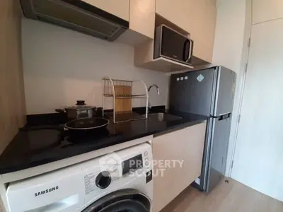 Modern compact kitchen with appliances including fridge, microwave, and washing machine in sleek design.