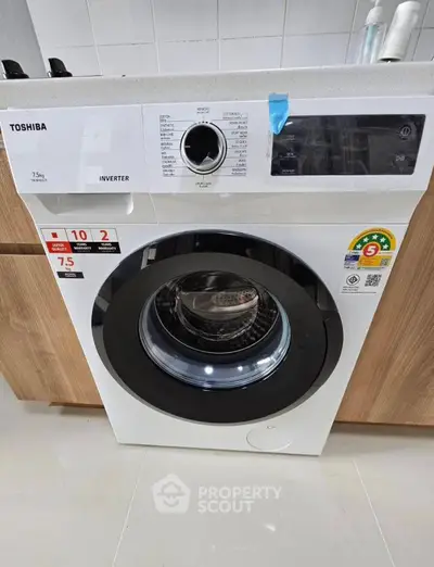 Modern washing machine in sleek kitchen setting with wooden cabinets.