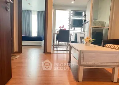 Modern apartment interior with wooden flooring, cozy living area, and view into bedroom and kitchen.