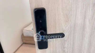 Modern smart lock on a wooden door with a glimpse of a cozy bedroom interior.
