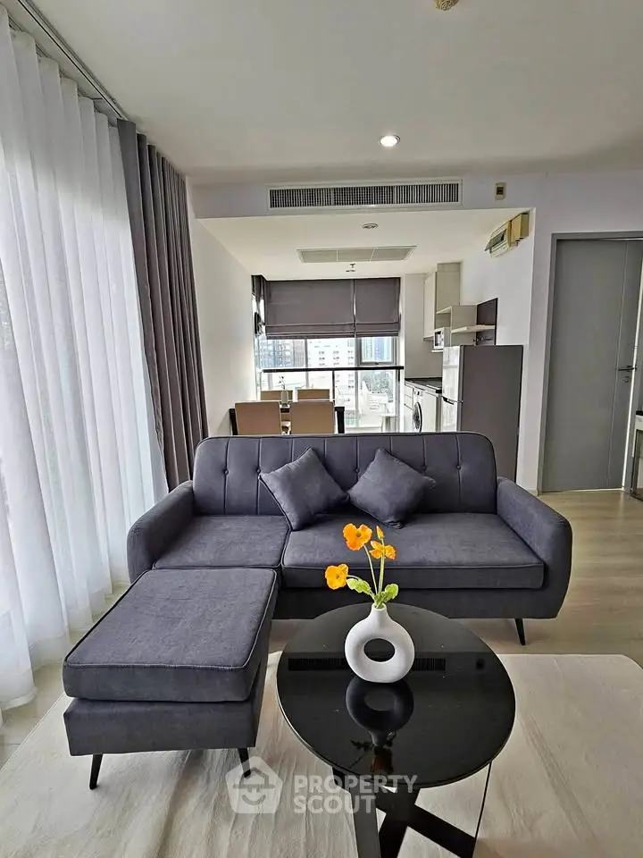 Modern living room with sleek furniture and open kitchen layout in a high-rise apartment.