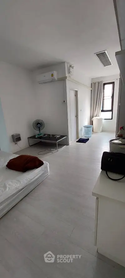 Bright and airy studio apartment with sleek white flooring, modern air conditioning unit, and ample natural light from large window.