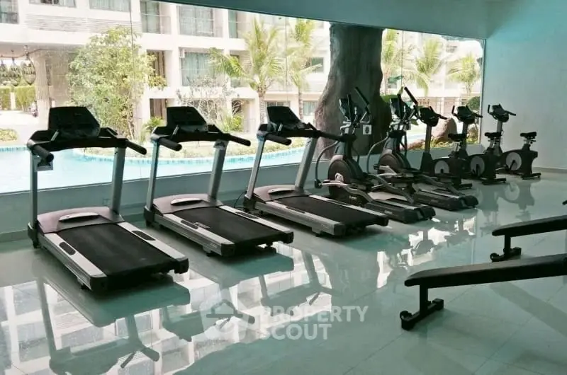 Modern gym with treadmills and exercise bikes overlooking a pool in a luxury residential complex.