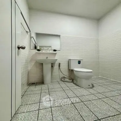 Spacious minimalist bathroom with tiled walls and floor, featuring a modern toilet and sink.