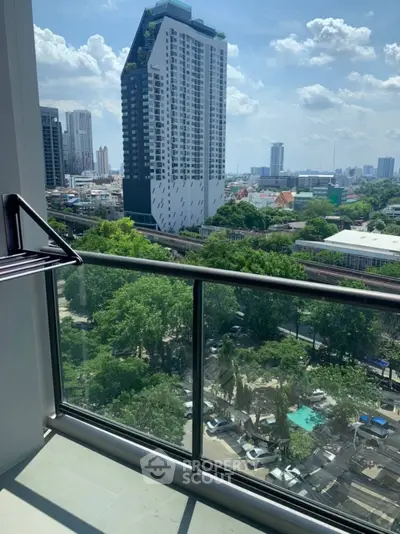 Stunning city view from a modern balcony with glass railing, showcasing urban skyline and greenery.