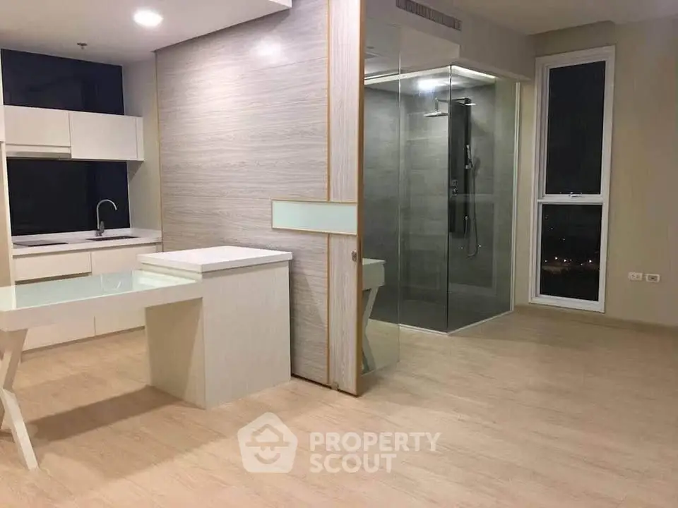 Modern open-plan living space with sleek kitchen and glass-enclosed shower area.