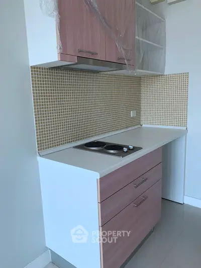 Modern compact kitchen with sleek cabinetry and electric cooktop in a stylish apartment.