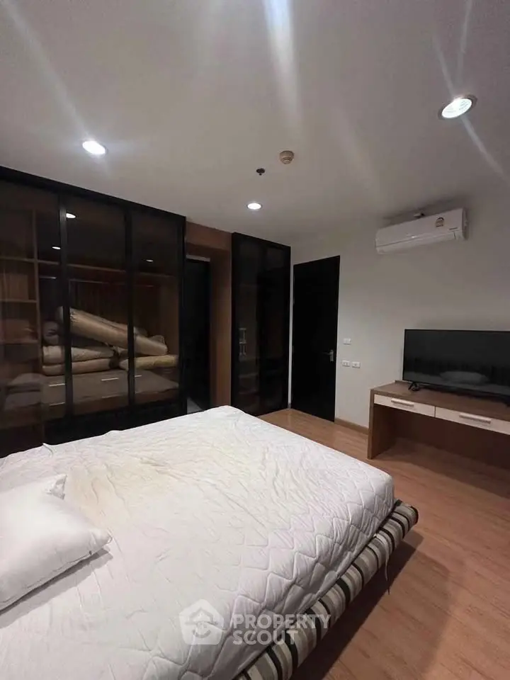 Modern bedroom with sleek design, featuring a comfortable bed, wall-mounted TV, and air conditioning unit.