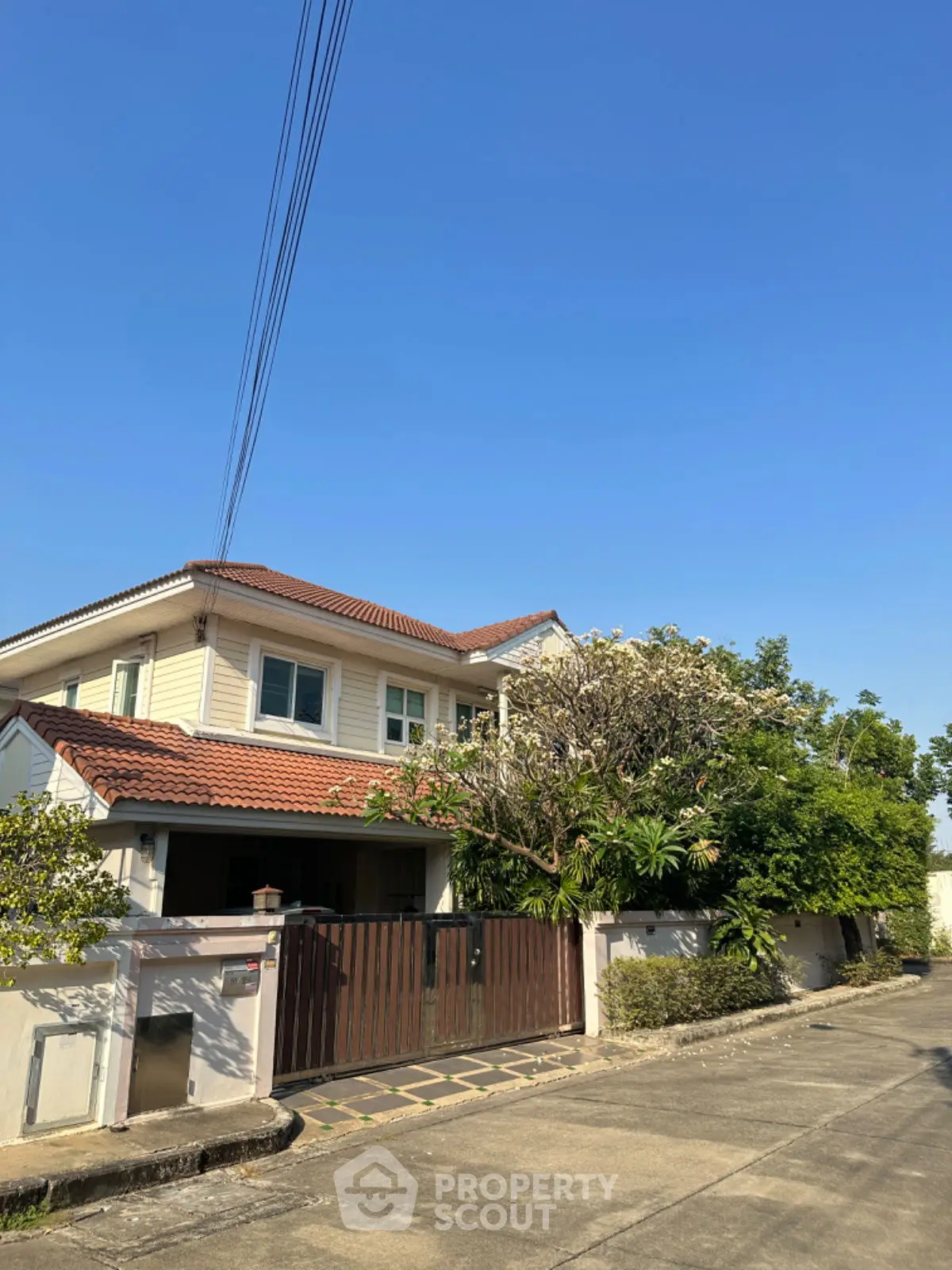 Charming two-story house with red-tiled roof and lush greenery in a serene neighborhood.