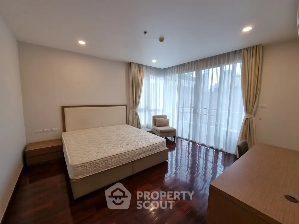 Spacious bedroom with large windows and wooden flooring in modern apartment