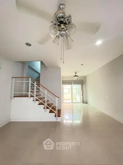 Spacious modern living room with ceiling fan and staircase, bright natural light