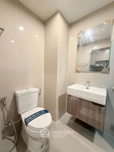 Modern bathroom with sleek fixtures and neutral tiles, featuring a toilet and vanity with a large mirror.