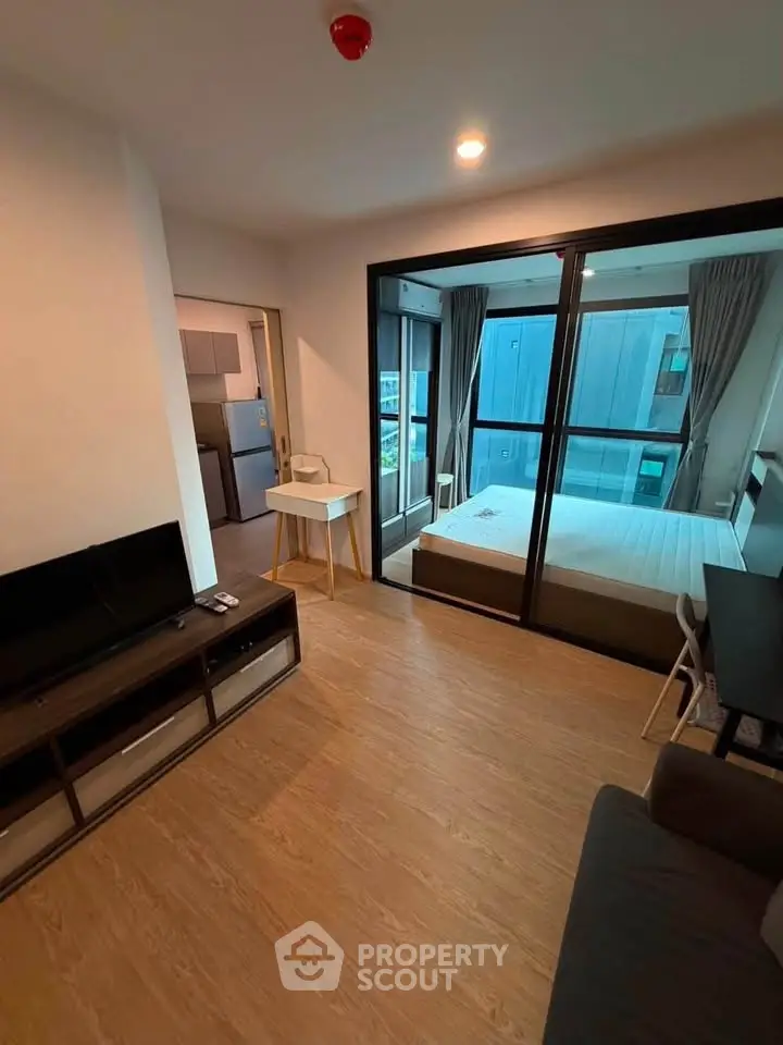Modern apartment interior with open living room and bedroom view, featuring sleek furniture and large windows.