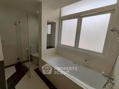 Modern bathroom with bathtub and glass shower enclosure, featuring frosted window for privacy.