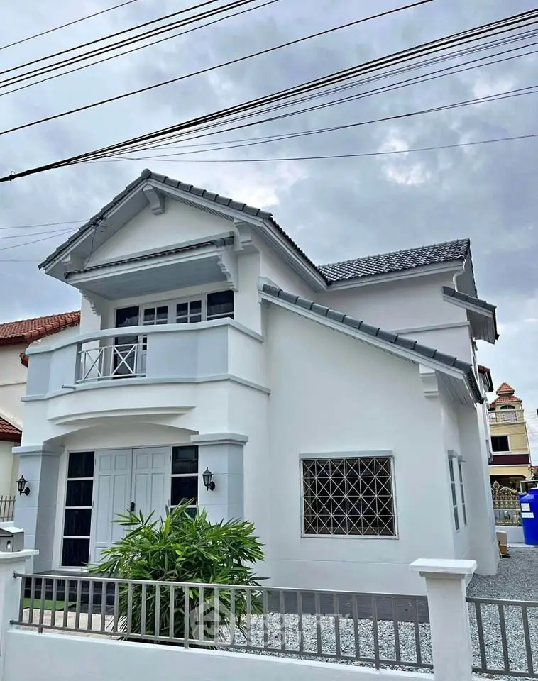 Charming two-story house with modern design and balcony, surrounded by a neat garden and secure fencing.