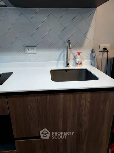 Modern kitchen with sleek sink and white countertop, featuring stylish wood cabinetry and herringbone backsplash.