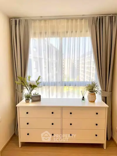 Bright bedroom with modern dresser and large window view in urban apartment.