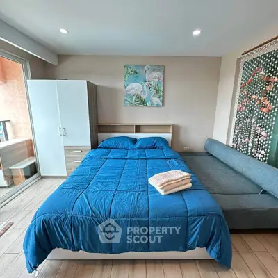 Modern bedroom with blue bedding, stylish decor, and natural light from balcony access.
