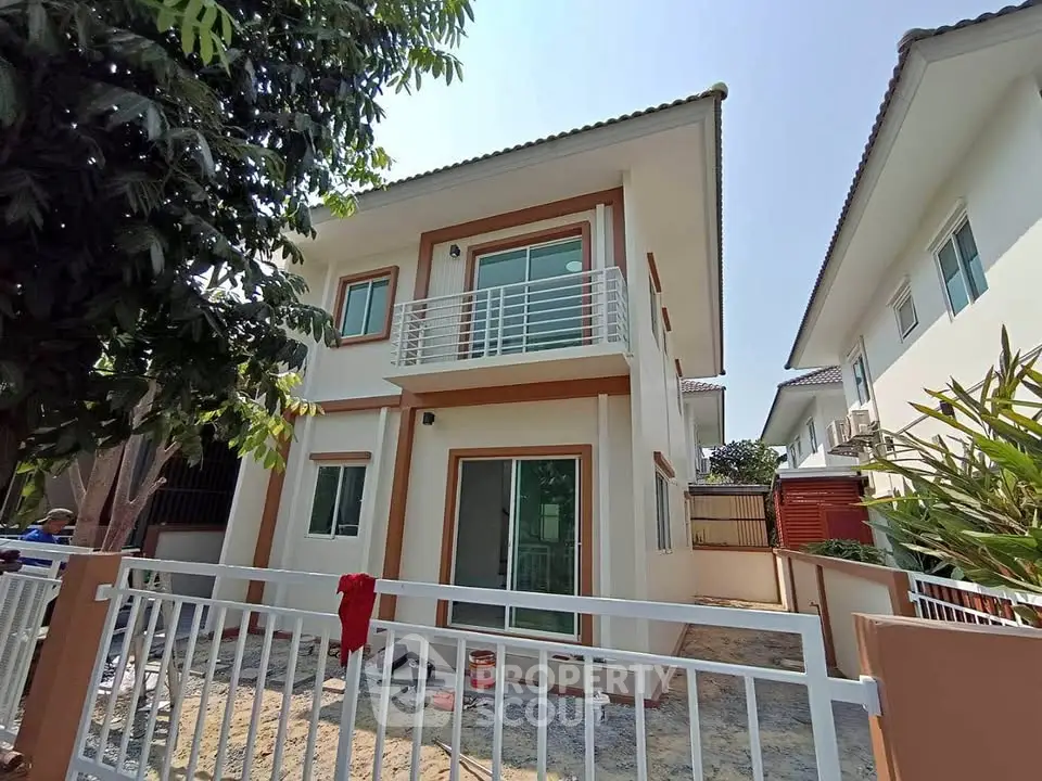 Modern two-story house with balcony and spacious yard in sunny neighborhood.