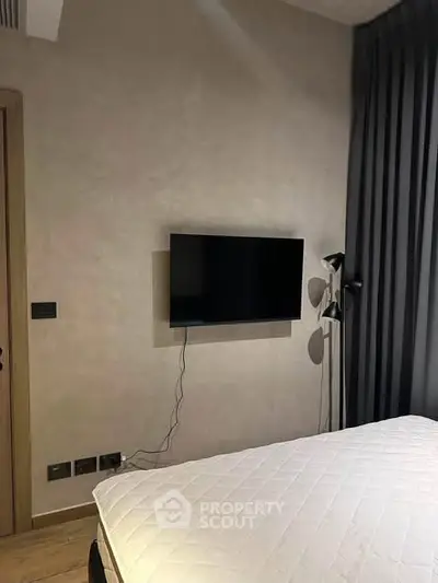 Modern bedroom with wall-mounted TV and stylish lighting, featuring a cozy bed and elegant curtains.