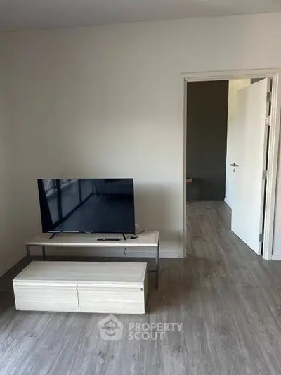 Modern living room with sleek TV stand and open doorway, showcasing minimalist design and wood flooring.