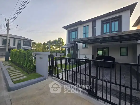 Modern two-story house with gated driveway and manicured lawn in a suburban neighborhood.