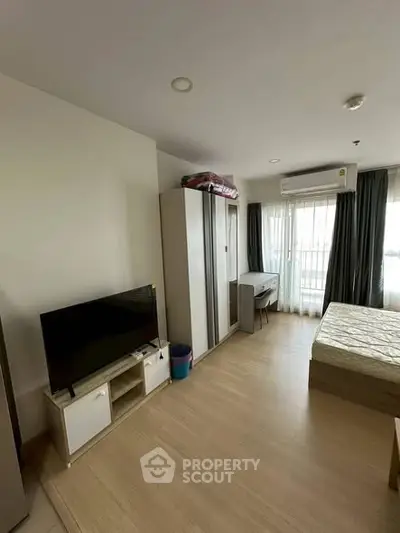 Modern bedroom with TV, wardrobe, and balcony access in a cozy apartment.