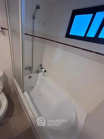 Modern bathroom with bathtub and window, featuring sleek tiles and contemporary fixtures.