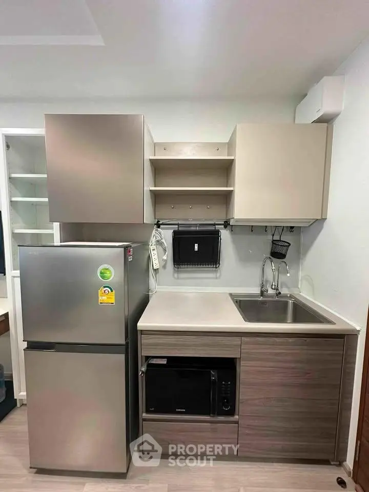 Modern compact kitchen with stainless steel fridge and microwave, sleek cabinetry, and efficient layout.