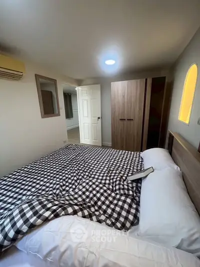 Cozy bedroom with modern wardrobe and checkered bedding, featuring a warm ambiance.