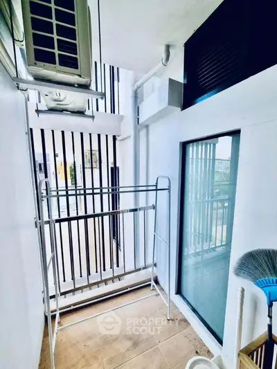 Compact balcony with laundry rack and air conditioning unit in modern apartment.